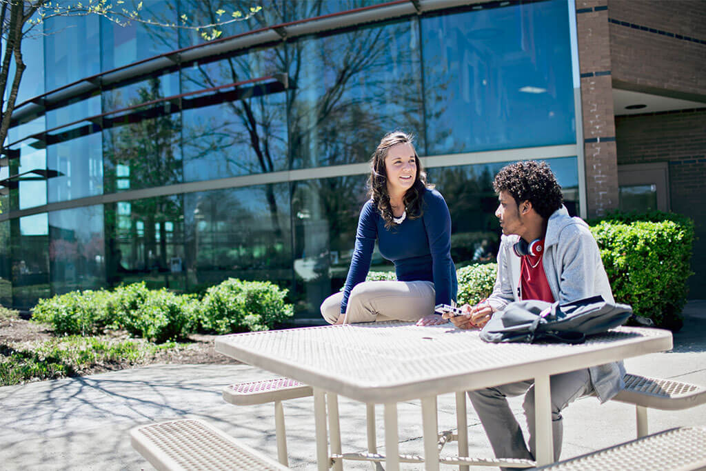 Two students sitting on picnic table outside building